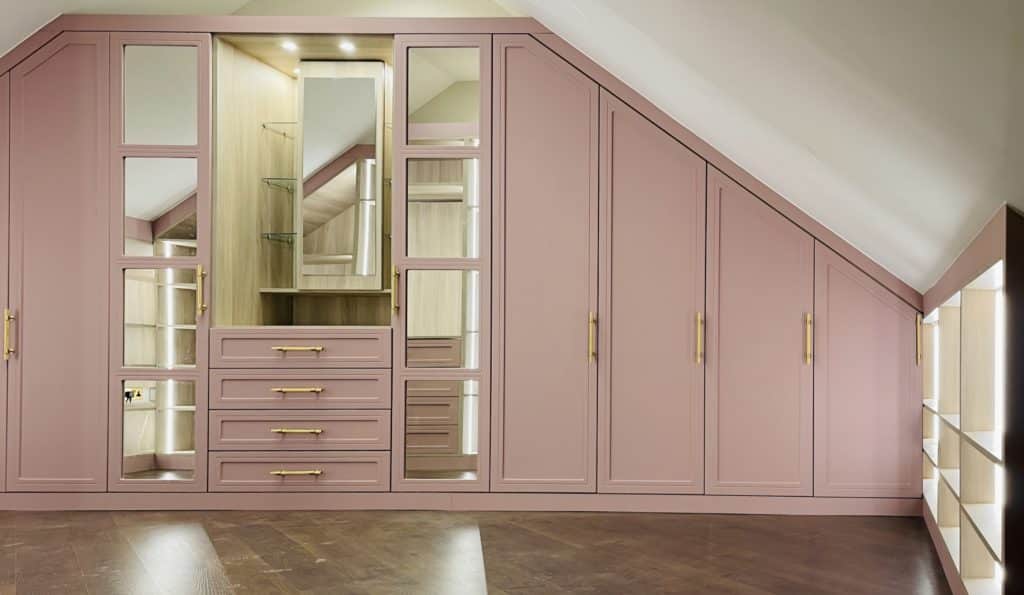 A bespoke attic bedroom in London with pink cabinets and mirrors designed by Mr Wardrobe.
